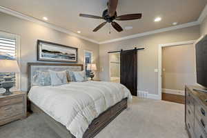 Carpeted bedroom featuring a barn door, a ceiling fan, crown molding, connected bathroom, and recessed lighting