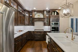 Kitchen featuring dark wood finish cabinetry, stainless steel appliances, hanging light fixtures, and dark wood-type flooring
