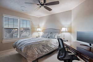 Carpeted bedroom with a ceiling fan, an office area, and a textured ceiling