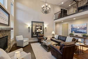 Living area featuring a stone fireplace, a high ceiling, dark wood-style floors, a chandelier, and a ceiling fan