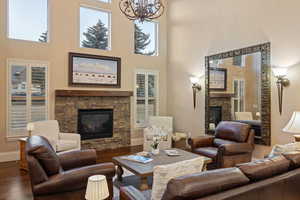 Living area with a fireplace, wood finished floors, a high ceiling, suspended lighting, and healthy amount of natural light