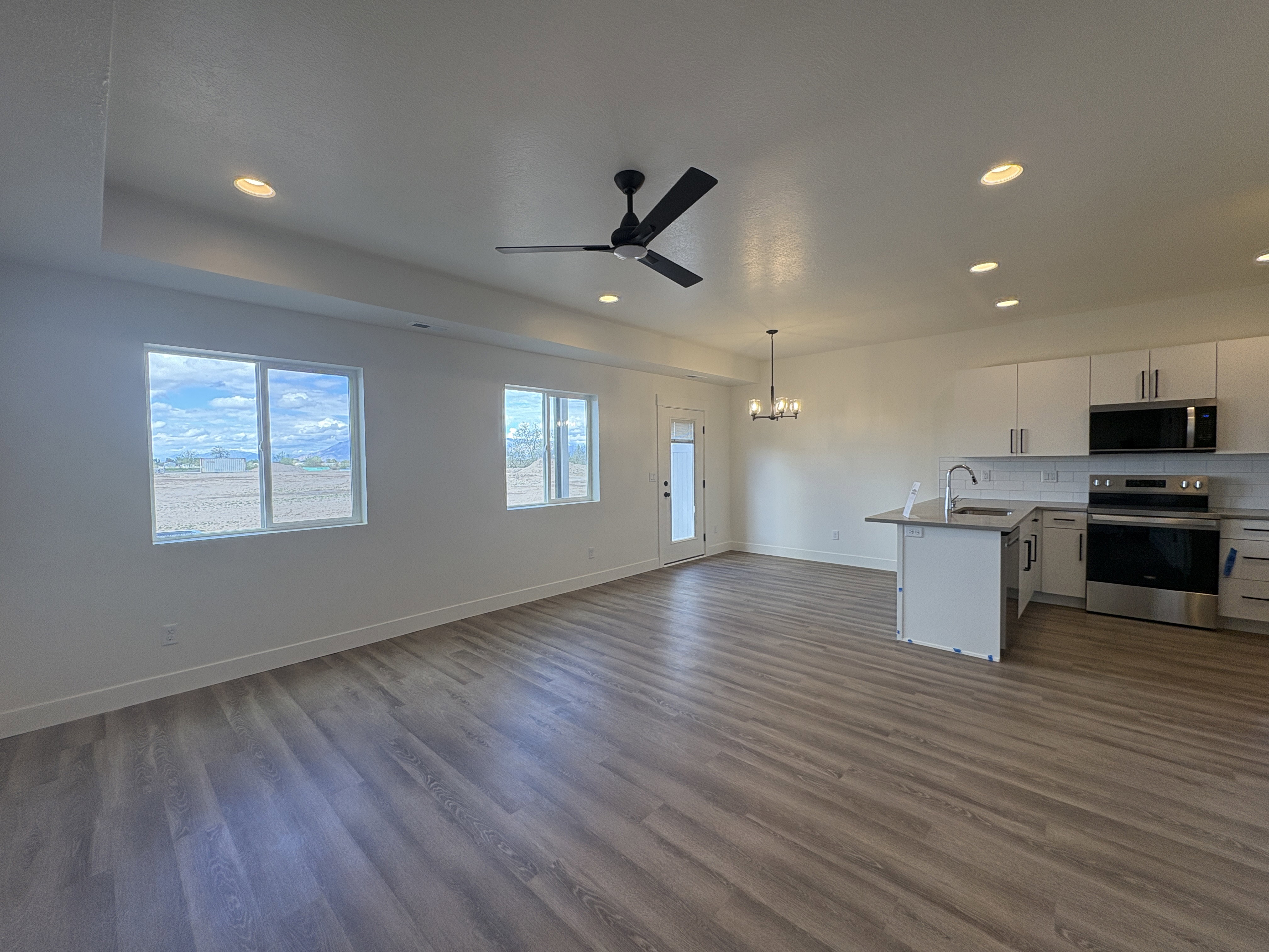 Kitchen featuring open floor plan, suspended lighting, stainless steel appliances, white cabinets, and a ceiling fan