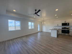 Kitchen featuring open floor plan, suspended lighting, stainless steel appliances, white cabinets, and a ceiling fan