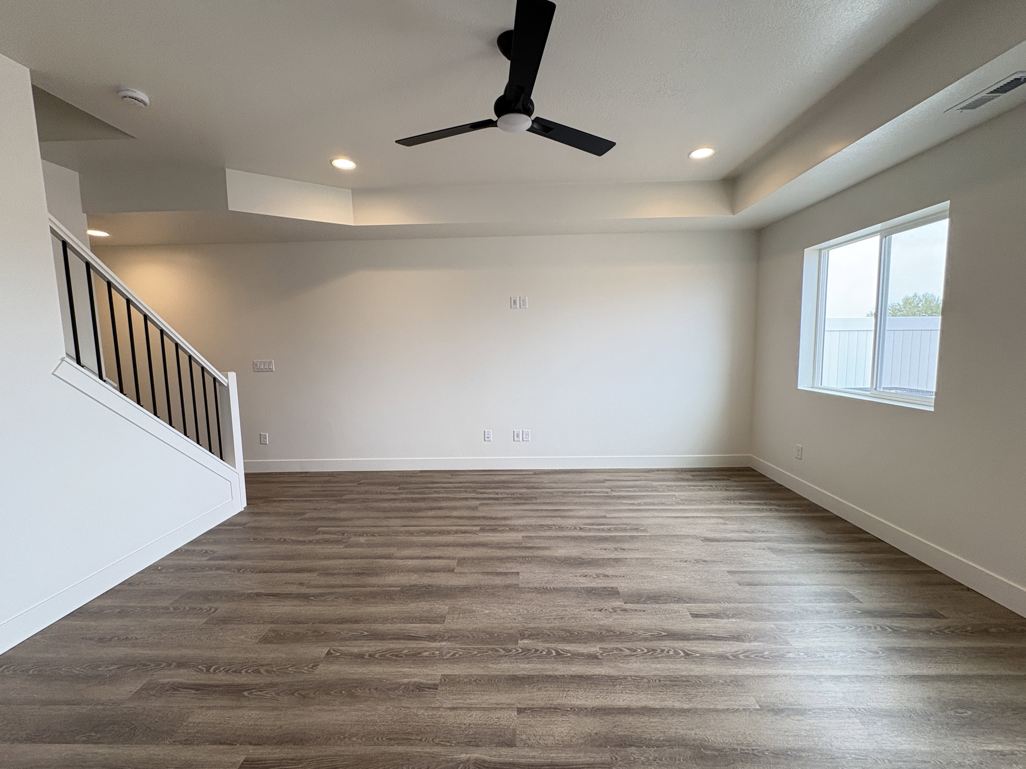 Unfurnished living room with a raised ceiling, ceiling fan, dark wood-style flooring, and recessed lighting