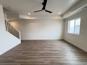 Unfurnished living room with a raised ceiling, ceiling fan, dark wood-style flooring, and recessed lighting