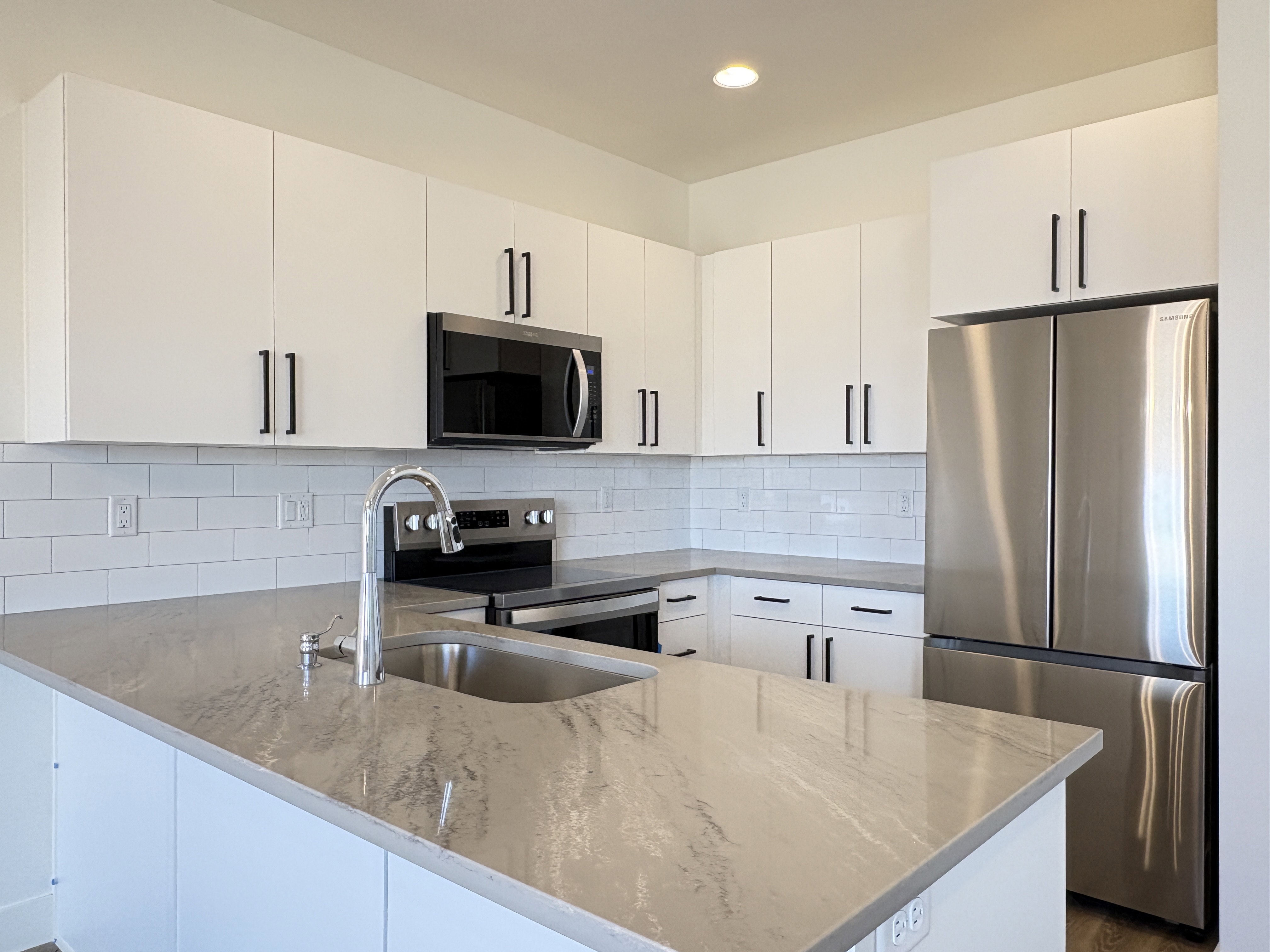 Kitchen with stainless steel appliances, white cabinets, a peninsula, light stone countertops, and decorative backsplash