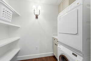 Laundry area with stacked washer / dryer, dark wood-type flooring, and cabinet space