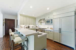 Kitchen with a kitchen breakfast bar, a peninsula, dark wood-type flooring, white cabinets, and crown molding