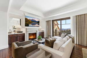 Living area with dark wood-style flooring, a warm lit fireplace, and a raised ceiling