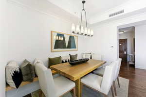 Dining area with dark wood finished floors, crown molding, and a raised ceiling