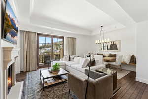 Living room with dark wood-type flooring, a fireplace, hanging lights, ornamental molding, and a raised ceiling