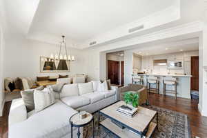 Living room with dark wood-style flooring, a tray ceiling, hanging lights, and crown molding