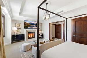 Bedroom with a glass covered fireplace, carpet floors, a raised ceiling, ornamental molding, and hanging lights