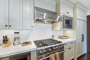 Kitchen featuring built in appliances, exhaust hood, white cabinetry, and light stone counters