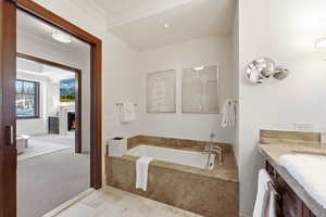 Bathroom with light carpet, a warm lit fireplace, vanity, a garden tub, and crown molding