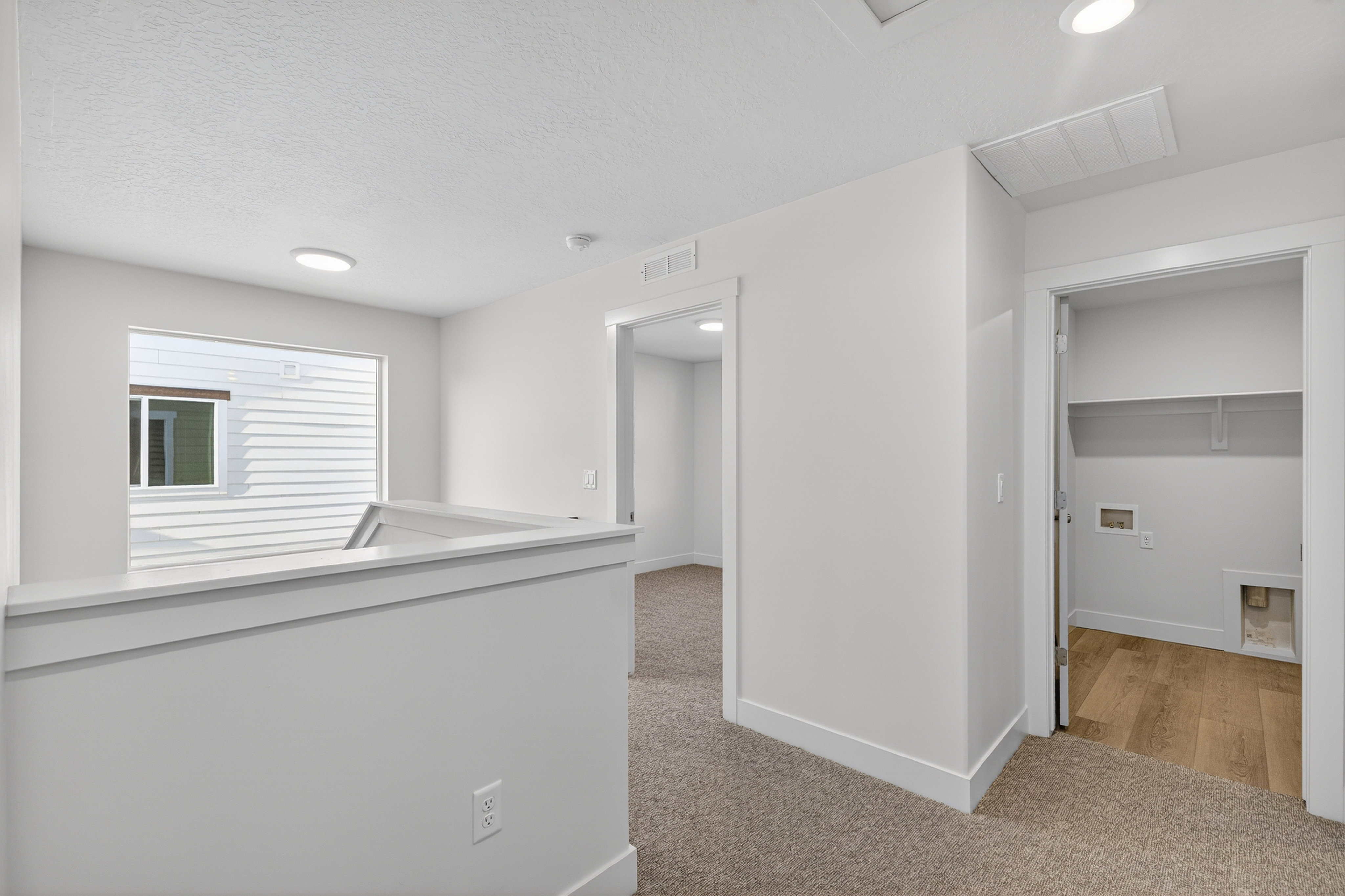 Upper-level hallway featuring a laundry closet with shelving, a window with exterior siding visible, light-colored carpet, and recessed ceiling lighting