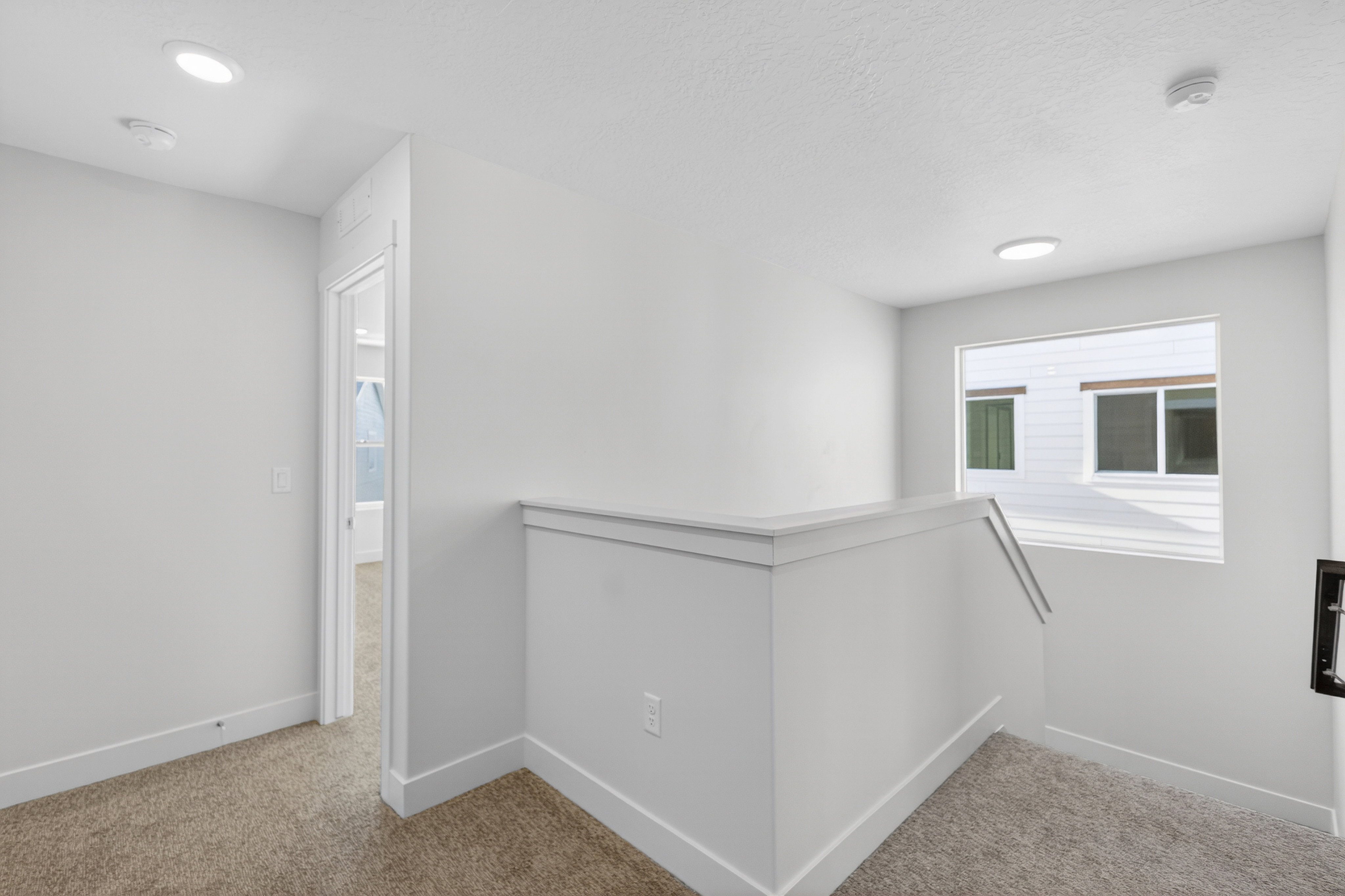 Upper-level landing featuring neutral carpeting, white trim, recessed lighting, and a prominent window