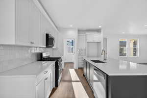Kitchen with stainless steel appliances, light wood-style flooring, an island with sink, two tone cabinetry, and light stone counters