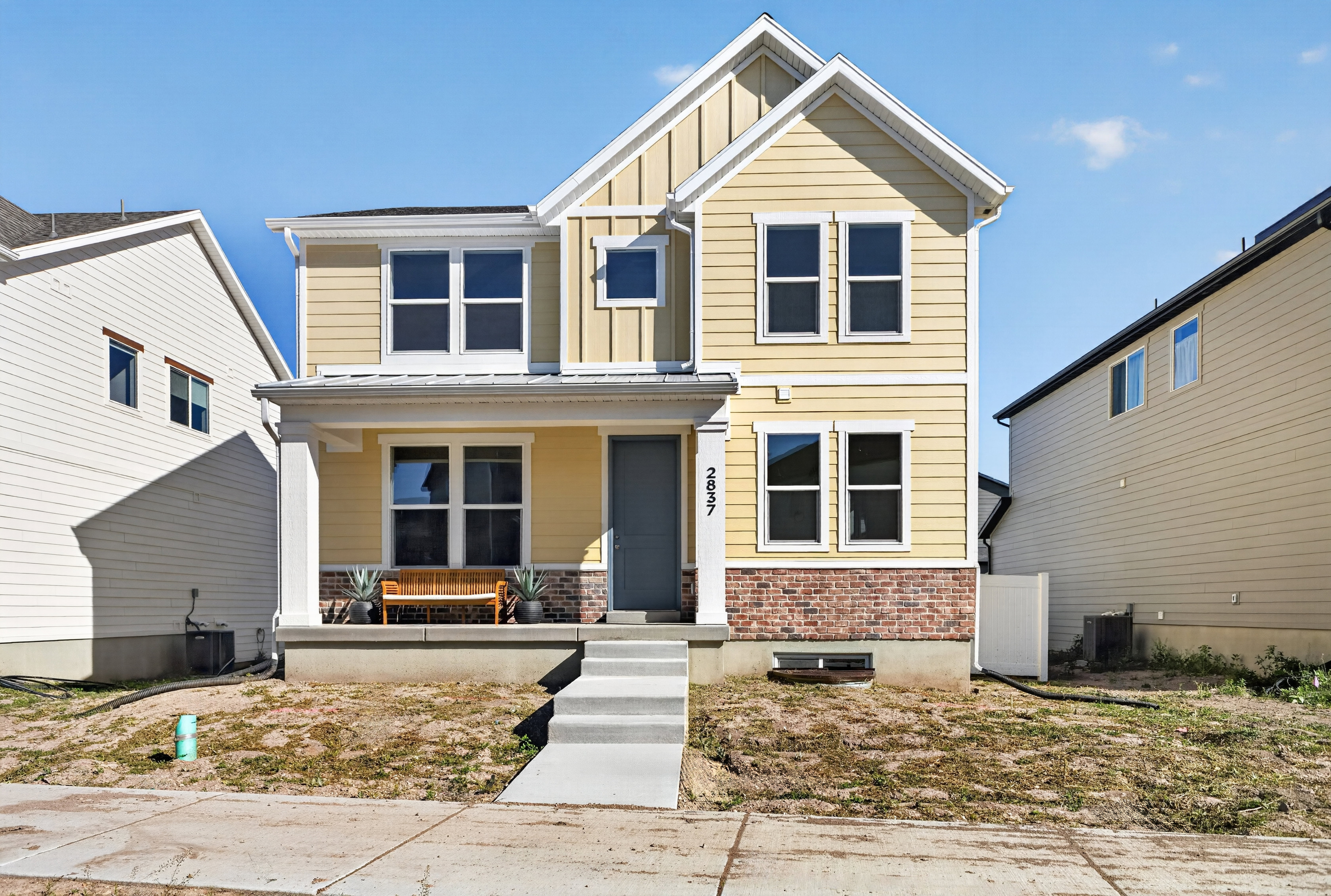 Two-story residence featuring light yellow horizontal siding and a red brick facade detail