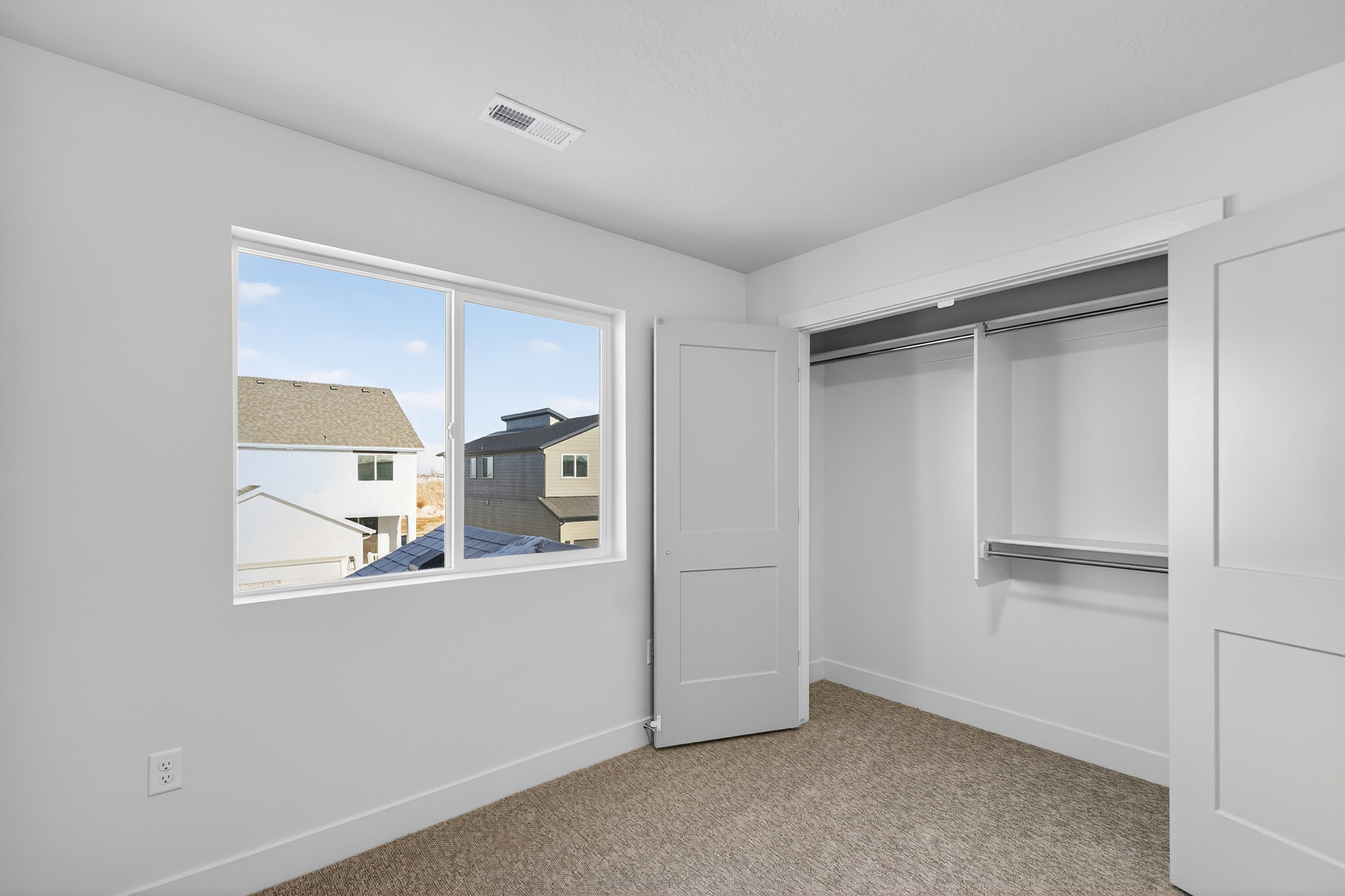 Room featuring a window, neutral-toned carpet, white baseboards, and a built-in closet with sliding panel doors and integrated shelving