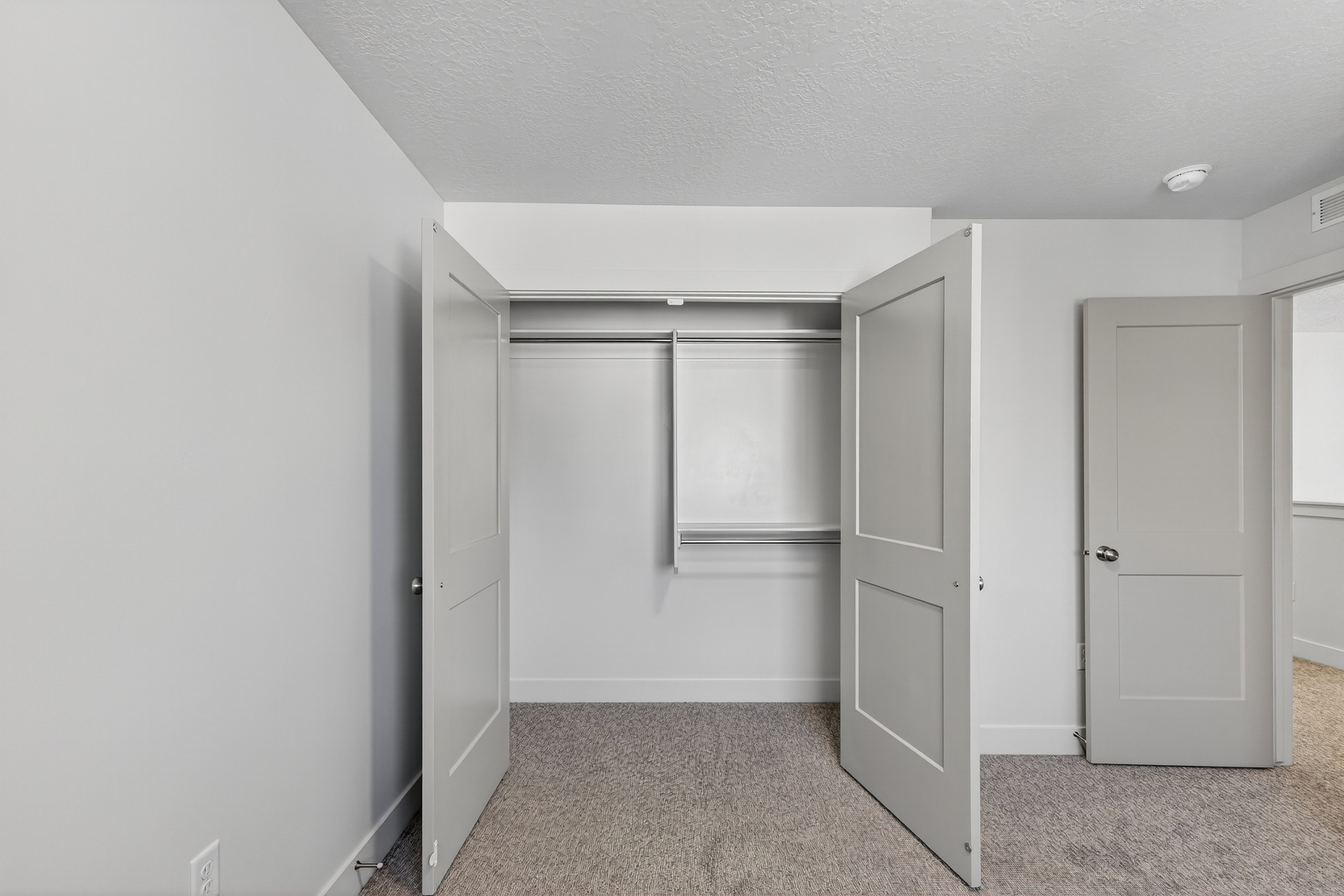Built-in closet featuring bi-fold doors, white shelving, and a hanging rod, set against light gray walls with a textured ceiling