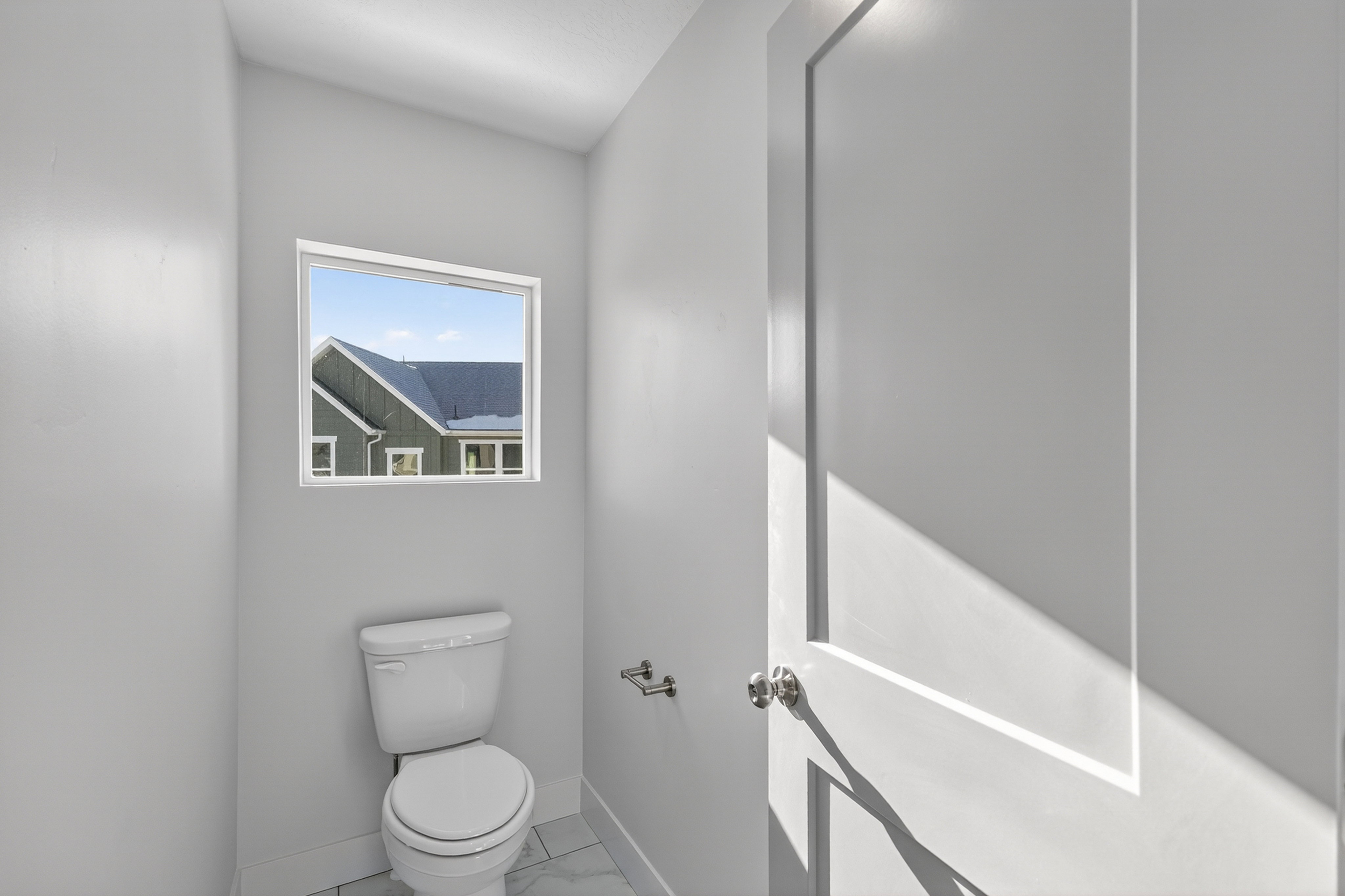 Powder room featuring a single toilet, a rectangular window, a panel door with a round knob, and tiled flooring