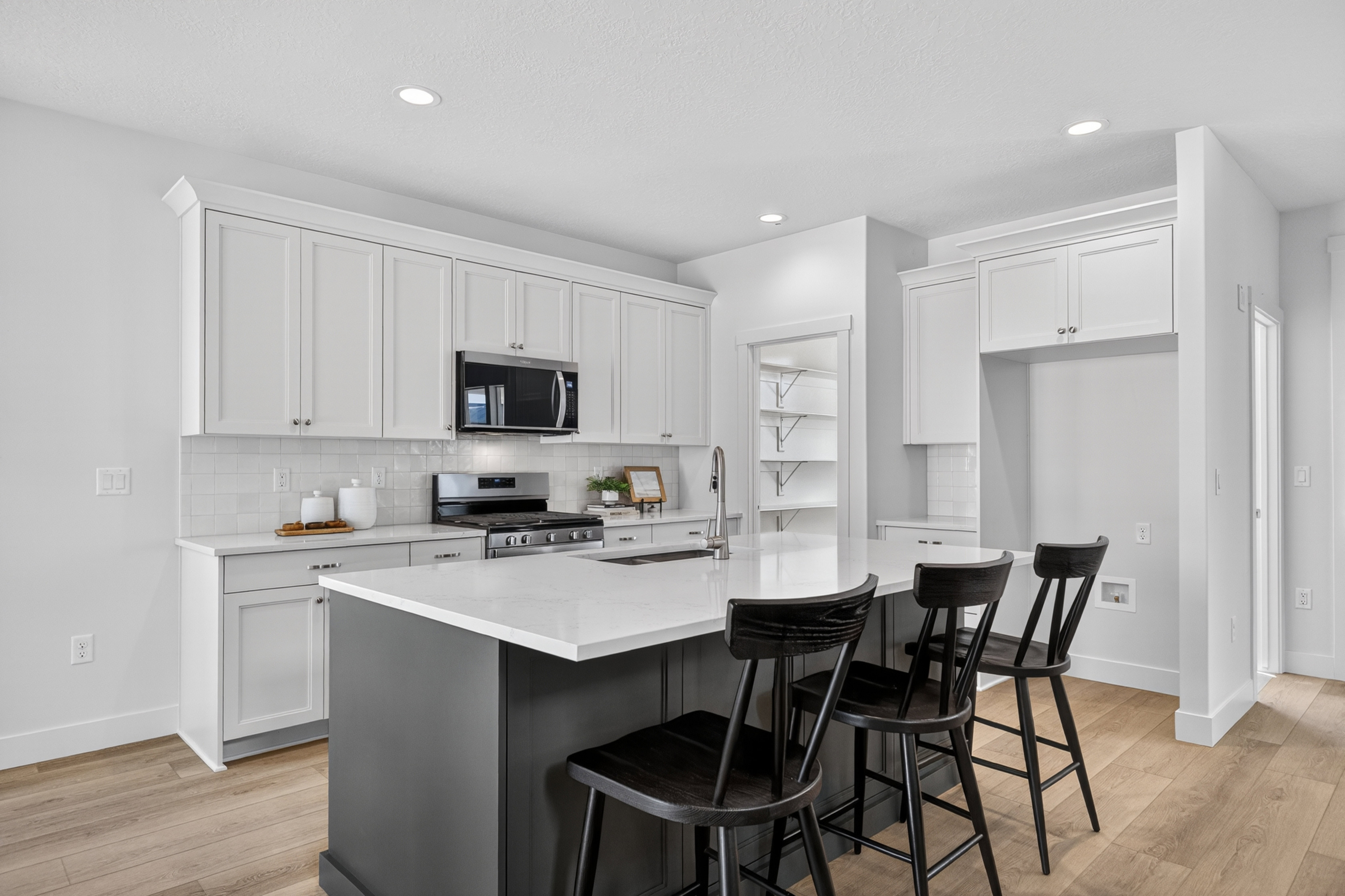 Modern kitchen featuring a central island with countertop seating, white shaker-style cabinetry, stainless steel appliances, a subway tile backsplash, and light wood-finish flooring