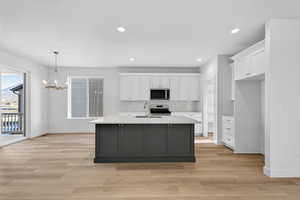 Kitchen with a kitchen island with sink, suspended lighting, light wood-style flooring, dual tone cabinetry, and stainless steel appliances