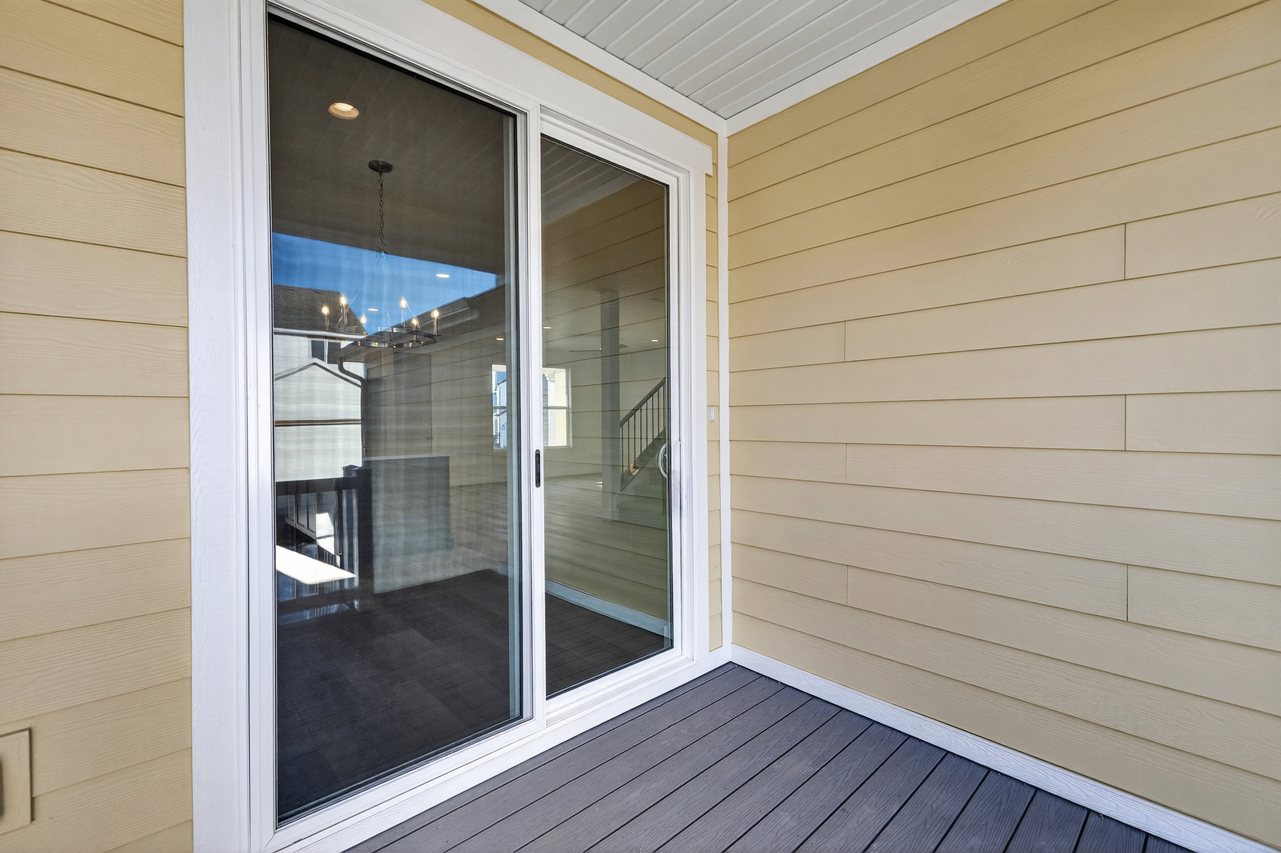 Sliding glass door leading to a balcony featuring composite decking, beige horizontal siding, and white soffit
