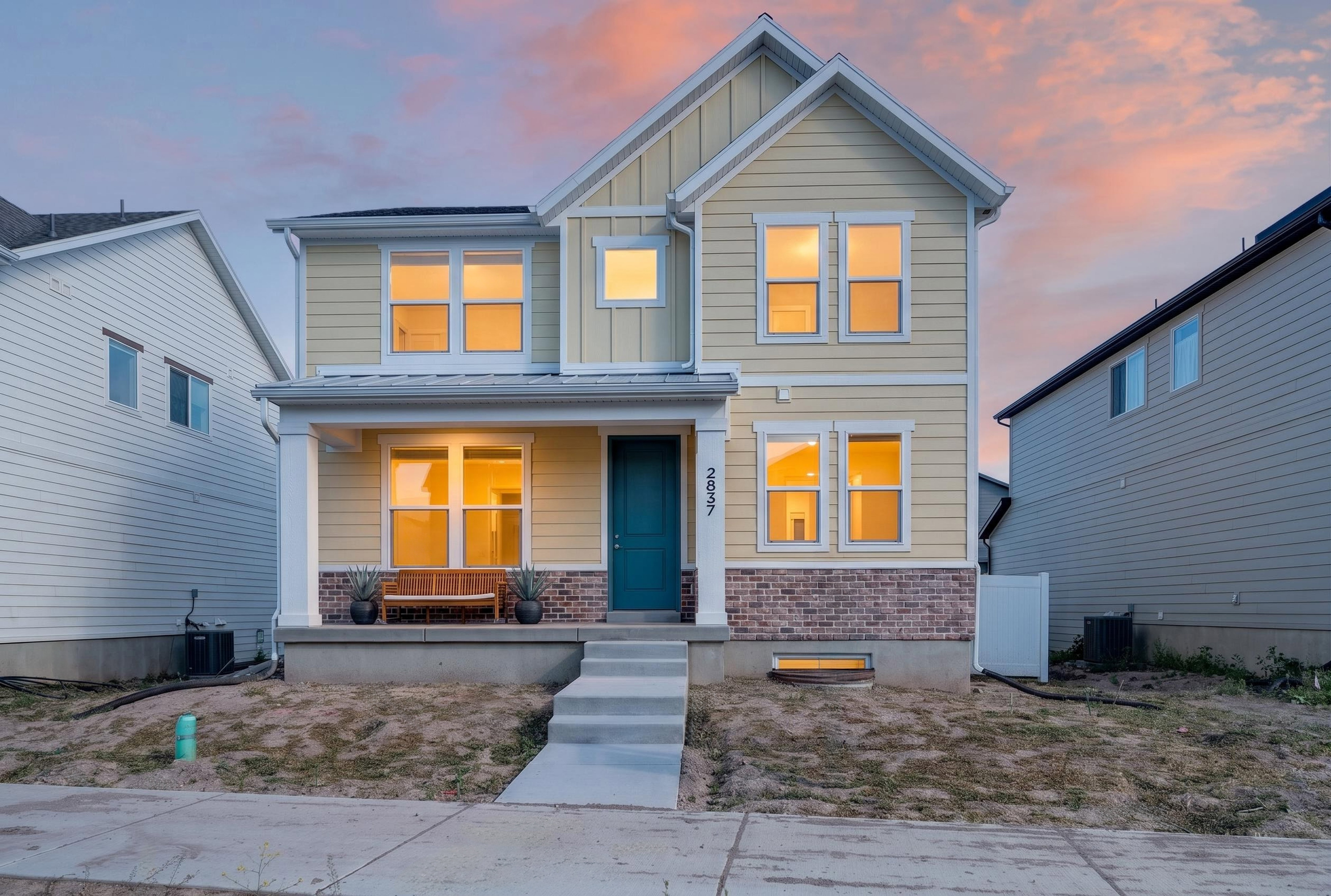 Contemporary two-story residence featuring light yellow siding, brick accents, a prominent teal front door, and a covered porch with white columns