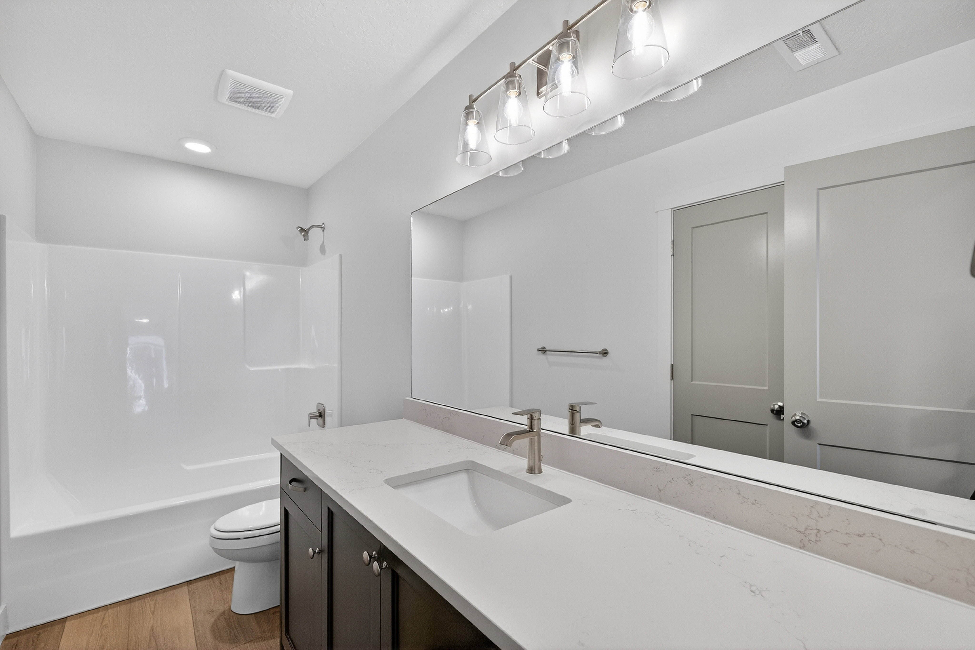 Bathroom featuring a white bathtub/shower combination, dark wood-finish vanity with a single basin, light-colored countertop, and brushed nickel fixtures