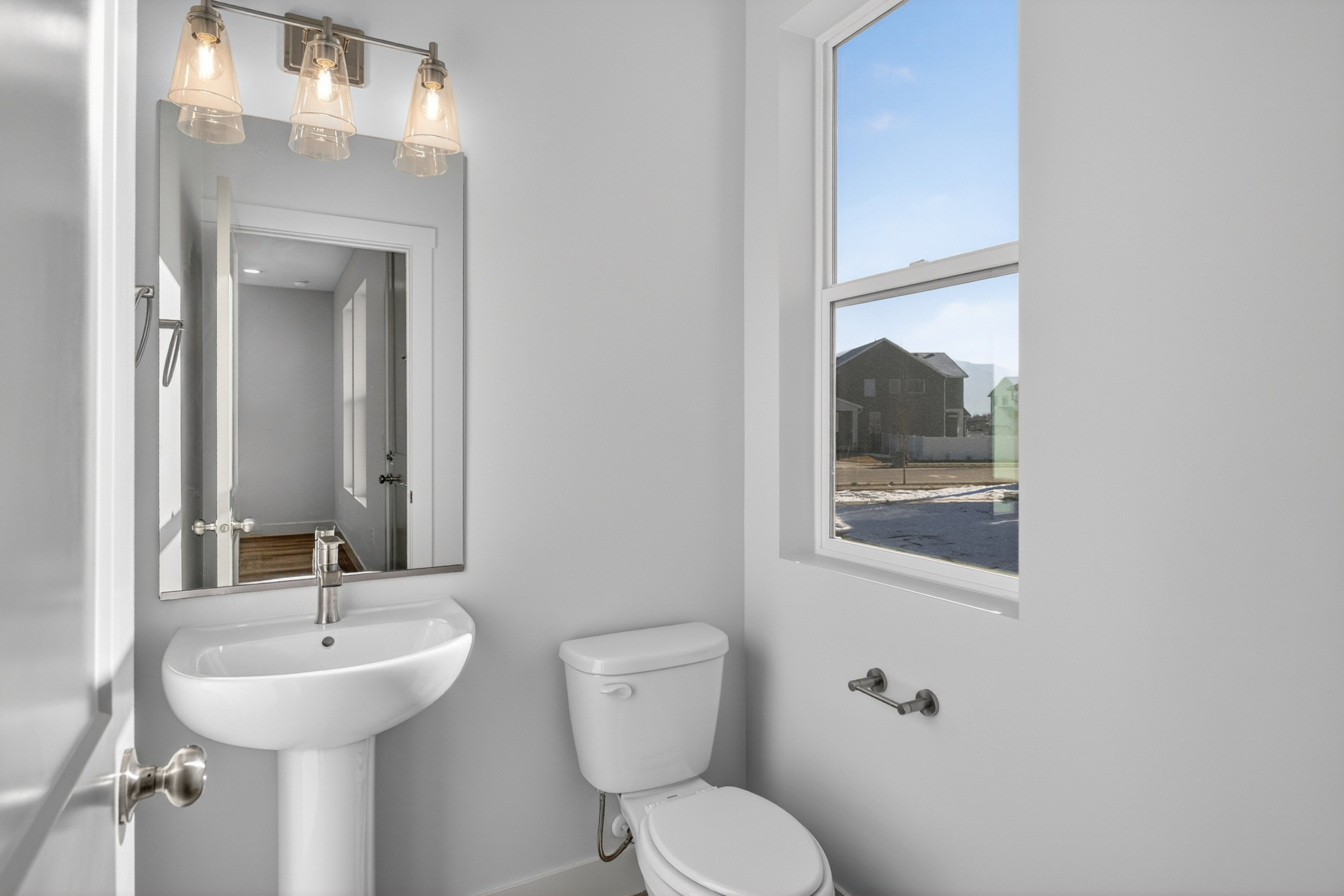 Bright bathroom featuring a pedestal sink, brushed nickel faucet, large mirror, and a three-light vanity fixture