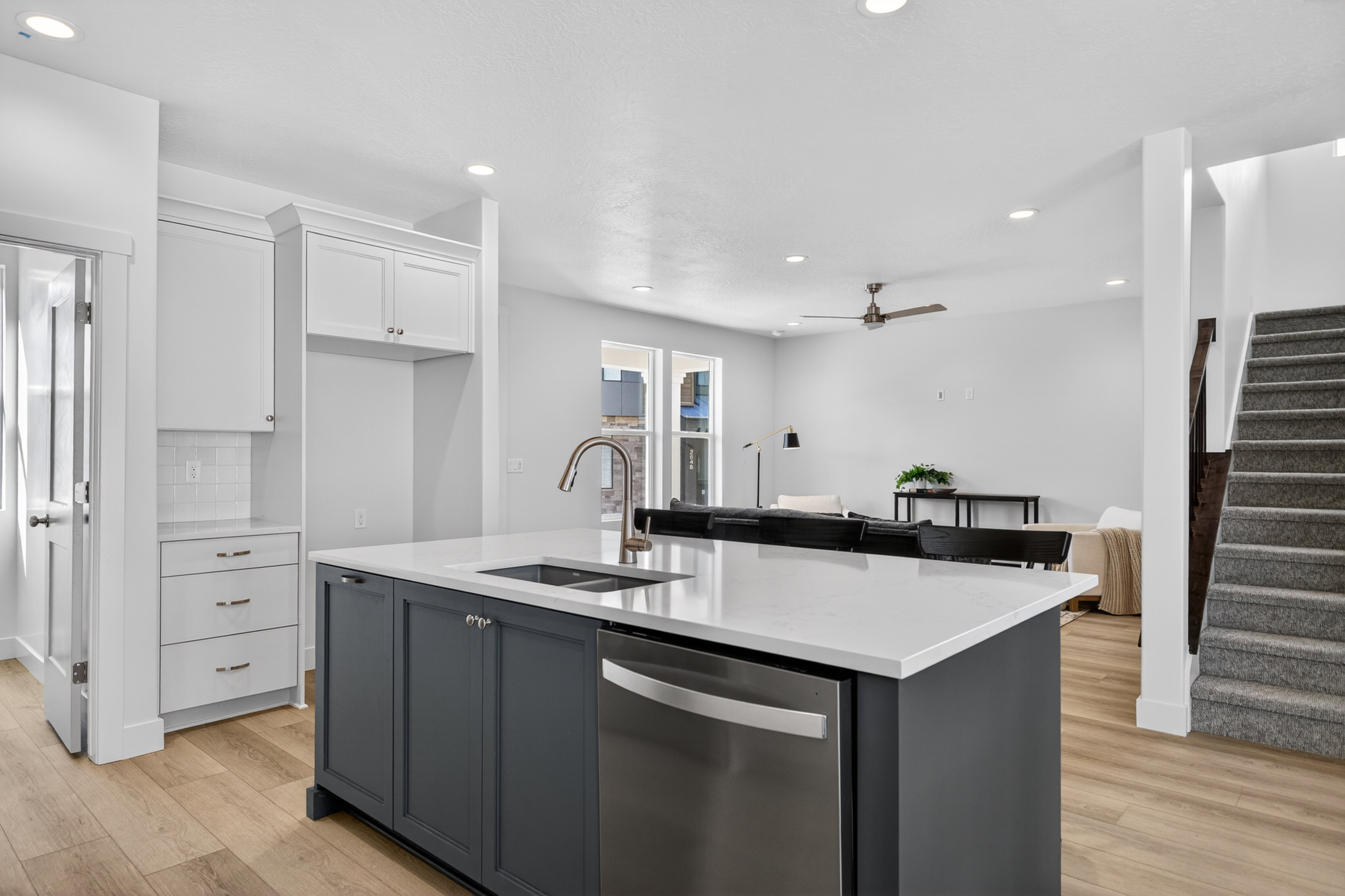 Open-concept kitchen featuring a dark blue island with a stainless steel sink and integrated dishwasher, light countertops, white cabinetry, and wood-finish flooring