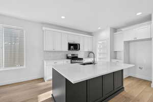 Dual tone kitchen featuring stainless steel appliances, light wood-style floors, dual tone cabinetry, light stone counters, and an island with sink