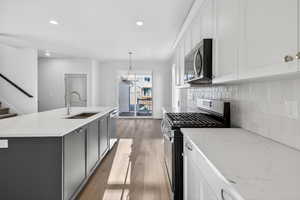 Two tone kitchen with stainless steel appliances, two tone cabinetry, light stone countertops, dark wood-style floors, and an island with sink