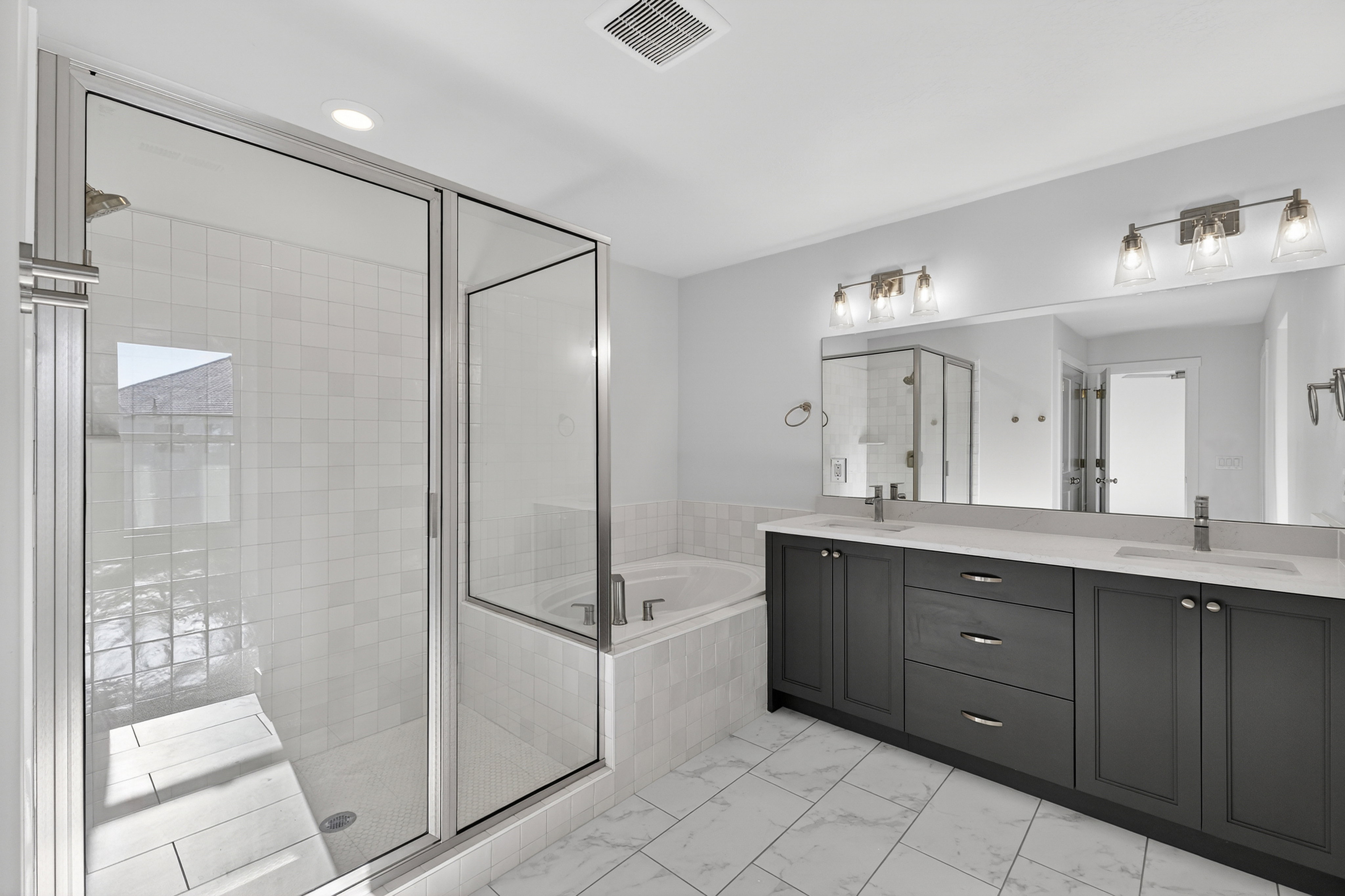 Spacious bathroom featuring a dual vanity with dark cabinetry and light countertops, a large mirror, and contemporary light fixtures