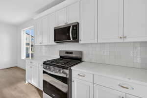 Kitchen featuring stainless steel appliances, white cabinets, light wood-type flooring, light stone counters, and backsplash