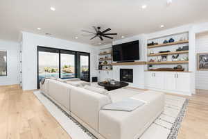 Living room featuring a fireplace, light wood-style floors, ceiling fan, built in features, and recessed lighting