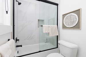 Full bathroom featuring toilet and combined bath / shower with glass door