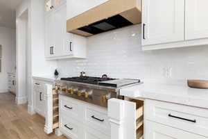 Kitchen featuring white cabinets, light stone countertops, stainless steel gas stovetop, and light wood-style flooring
