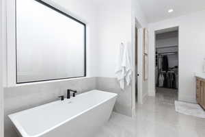 Full bath with a spacious closet, vanity, a freestanding bath, tile walls, and recessed lighting