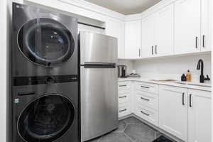 Laundry area featuring dark tile patterned flooring and stacked washer and dryer