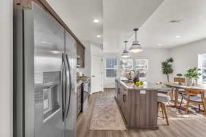 Kitchen with stainless steel fridge, light stone countertops, decorative light fixtures, light wood-style floors, and a breakfast bar