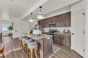 Kitchen featuring light stone countertops, a kitchen island with sink, stainless steel appliances, pendant lighting, and a breakfast bar area