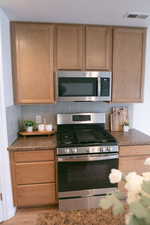 Kitchen with stainless steel appliances, decorative backsplash, dark stone counters, and wood finished floors
