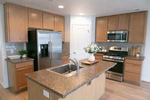 Kitchen featuring stainless steel appliances, dark countertops, light wood-style floors, a center island with sink, and recessed lighting