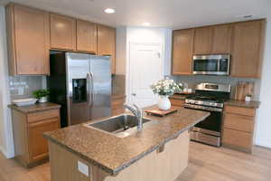 Kitchen featuring stainless steel appliances, dark countertops, light wood finished floors, a center island with sink, and recessed lighting