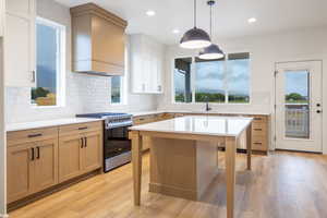 Two tone kitchen featuring two tone cabinets, gas stove, tasteful backsplash, light wood-style floors, and decorative light fixtures