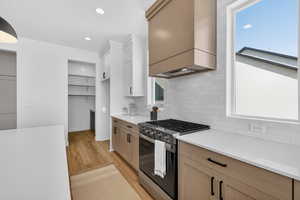 Kitchen featuring gas stove, light wood finished floors, decorative backsplash, light stone countertops, and dual tone cabinets