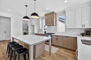 Dual tone kitchen with stainless steel range with gas stovetop, light wood-style floors, light stone countertops, a center island, and dual tone cabinets